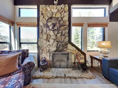 a stone fireplace in a living room with a blue couch at Remodeled Spacious Cozy Condo Great For Families! in Mammoth Lakes