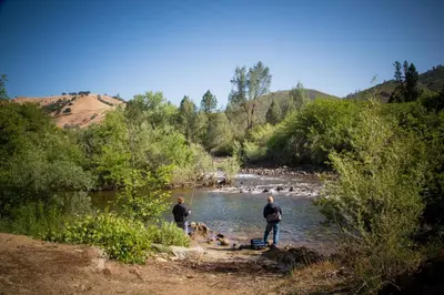 two men and a dog standing in a river at Ponderosa Camping Resort One-Bedroom Cabin 2 in Lotus