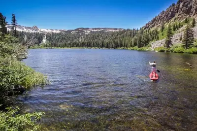 a person is standing on a paddle board in a river at Mammoth Ski & Racquet 124 in Mammoth Lakes