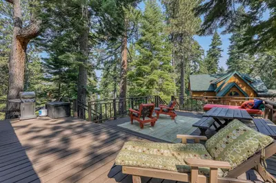 a deck with furniture and a cabin in the woods at The Cherry Leaf Lodge & Retreat on Fallen Leaf Lake in Fallen Leaf