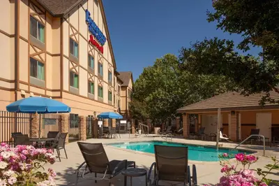 a hotel with a pool and chairs and umbrellas at Fairfield Inn & Suites by Marriott Selma Kingsburg in Kingsburg