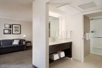 a bathroom with a sink and a living room at Sonesta ES Suites Fresno in Fresno