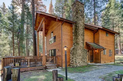 a log cabin in the woods with a large tree at 12 Cabin Twelve in Wawona
