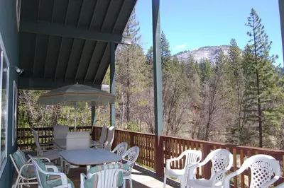a deck with white chairs and a table and an umbrella at 44R Grant's Camp in Wawona