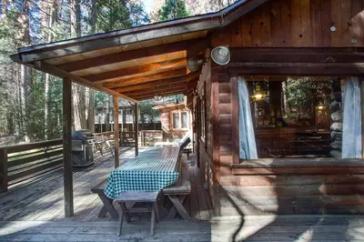 a wooden cabin with a picnic table on a deck at 53 Creekside Cabin in Wawona