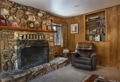 a living room with a stone fireplace and a chair at 23 Arnetts Cabin in North Wawona