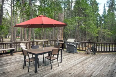 a table and chairs with an umbrella on a deck with a grill at 42R Rosenberg's Creekside Cabin in Wawona