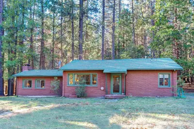 a small red house in the middle of a forest at 81 Ashbaugh Meadow in North Wawona