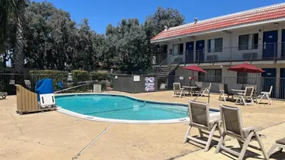 a swimming pool with chairs and tables and a building at Motel 6 Modesto, CA in Modesto