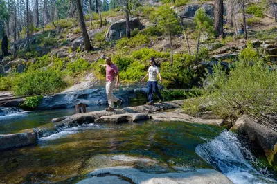 two people are crossing a stream in a river at Tenaya at Yosemite in Fish Camp