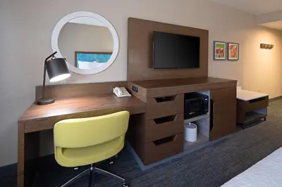 a hotel room with a desk with a mirror and a yellow chair at Hampton Inn Visalia in Visalia