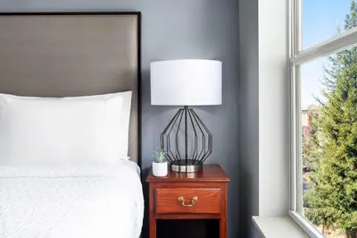 a bed with a lamp on a nightstand next to a window at Homewood Suites by Hilton Sacramento/Roseville in Roseville