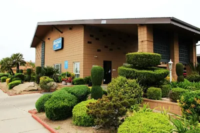 a building with a bunch of trees and bushes at Rodeway Inn Near University-Gateway to Yosemite in Merced