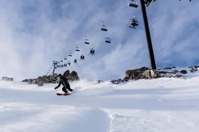 a person riding a snowboard down a snow covered slope with a ski lift at Chateau De Montagne #24 Condo in Mammoth Lakes