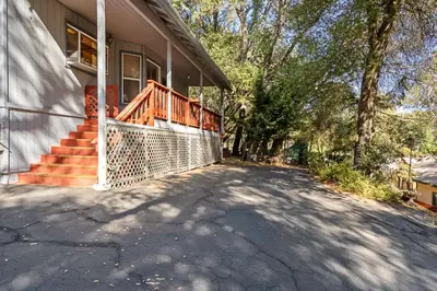 a house with a porch with a fence on a driveway at Yosemite Falls Calling in Groveland
