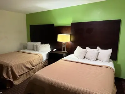 two beds in a hotel room with a green wall at Hollister Inn in Hollister