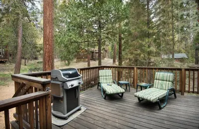 a grill and chairs on a deck with trees at 16 Chipmunks Holiday in Wawona