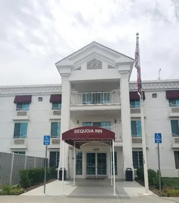 a large white building with a flag in front of it at Sequoia Inn in Hanford