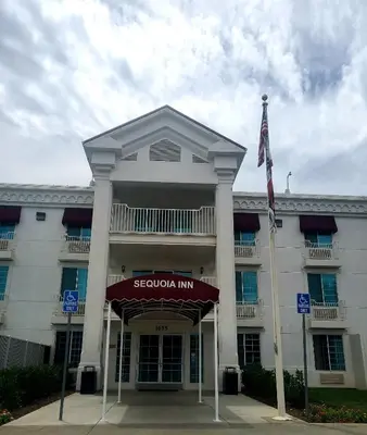 a large white building with a flag in front of it at Sequoia Inn in Hanford
