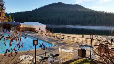a swimming pool with tables and chairs next to a lake at The Pines Resort & Conference Center in Bass Lake