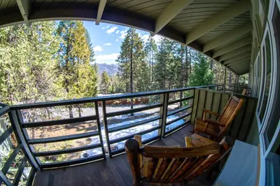 two rocking chairs on a porch with a view of the woods at Narrow Gauge Inn in Fish Camp
