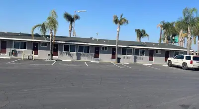 a parking lot in front of a building with palm trees at King's Inn Motel in Kingsburg