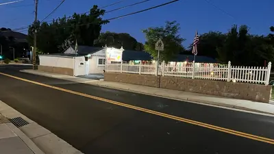 a white fence and a white house with a flag at Jumping Frog Motel in Angels Camp