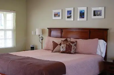 a bedroom with a large bed with pink sheets and pillows at Queen's Inn By The River in Oakhurst