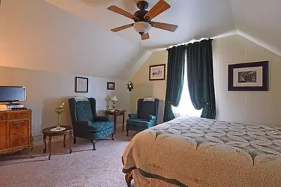 a bedroom with a bed and two chairs and a ceiling fan at B Street House Inn in Virginia City