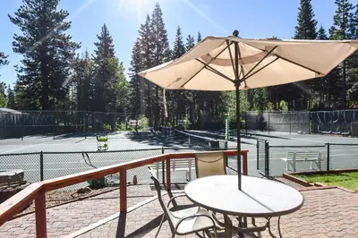 a table and chair with an umbrella on a tennis court at Ski Trails 4024 in Truckee