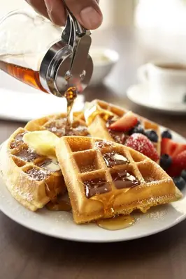 a person is pouring syrup onto a plate of waffles at Country Inn & Suites by Radisson, Fresno North, CA in Fresno