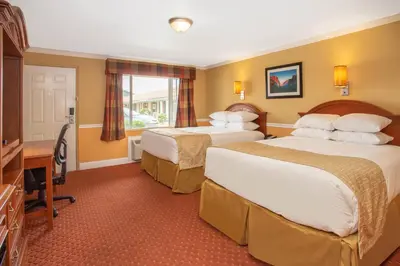 a hotel room with two beds and a desk at Travelodge by Wyndham Hawthorne in Hawthorne