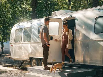 a man and a woman standing outside of a trailer with a dog at AutoCamp Yosemite in Midpines
