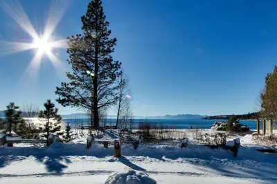 a snow covered field with a tree and the sun at Peaceful Forest Retreat in Carnelian Bay