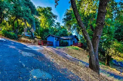 a house on the side of a road next to a tree at NEW! Cozy & Secluded House w/Deck - Near Yosemite! in Tuolumne
