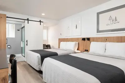 two beds in a hotel room with white walls at Hotel Lumberjack - Sonora in Sonora