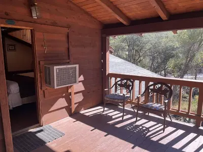 a porch of a cabin with a bed and two chairs at Whispering Pines Lodge in Kernville