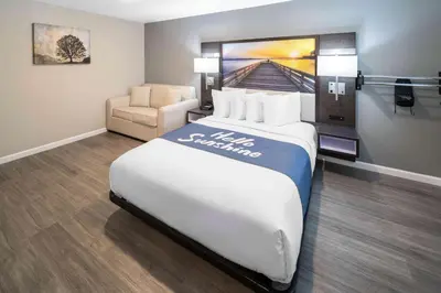 a hotel room with a large bed and a chair at Days Inn by Wyndham Galt - Elk Grove South in Galt