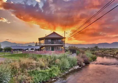 a house on the side of a river with a sunset at Walker River Lodge in Bridgeport