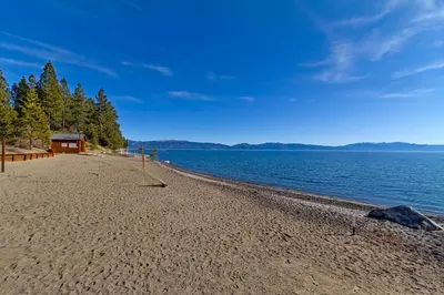 a sandy beach next to a body of water at Sunny Daze at Dollar Point by Tahoe Getaways - Tahoe Classic w Open Floor Plan, Wood Fireplace, Close to Lake! in Tahoe City