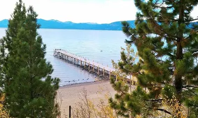 a dock in the water next to a beach at Sunny Daze at Dollar Point by Tahoe Getaways - Tahoe Classic w Open Floor Plan, Wood Fireplace, Close to Lake! in Tahoe City