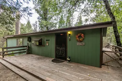 a green house with a deck in the woods at Yosemite Cabin in Wawona