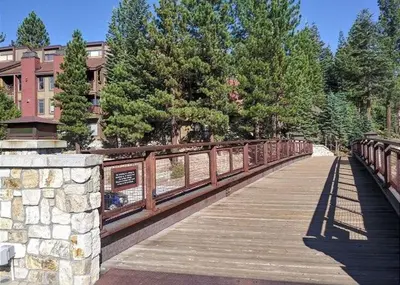 a wooden bridge over a river with trees and a building at Val D'Isere #1 Condo in Mammoth Lakes