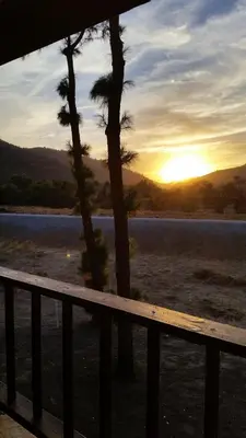 a sunset over a lake with a fence and trees at Western Holiday Lodge in Three Rivers
