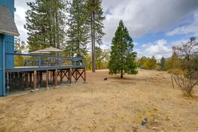 a house with a deck next to a tree at 7 Mi to Bass Lake! Spacious Mudge Ranch Retreat in Coarsegold