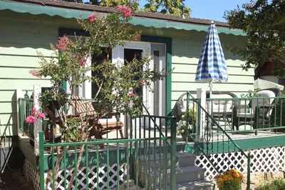 a green house with a porch and an umbrella at Kern Riverview Inn in Kernville