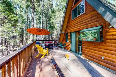 a wooden deck with an orange umbrella and chairs at Under The Trees in Camp Connell