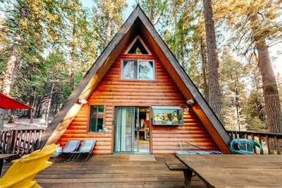 a cabin with a gambrel roof on a wooden deck at Under The Trees in Camp Connell