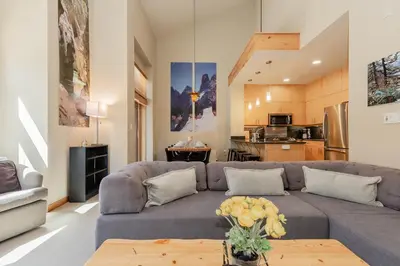 a living room with a gray couch and a kitchen at Solstice 24 in Mammoth Lakes