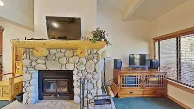 a living room with a stone fireplace with a tv on top at Cozy One Bedroom Condo with Loft! in Mammoth Lakes
